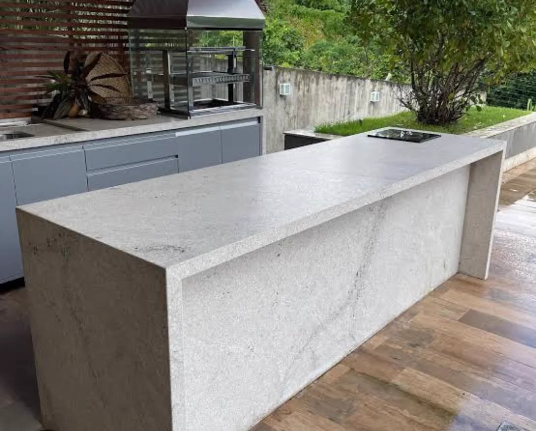 Ilha com pé lateral em granito Branco Itaúnas escovado e recorte para cooktop em espaço gourmet