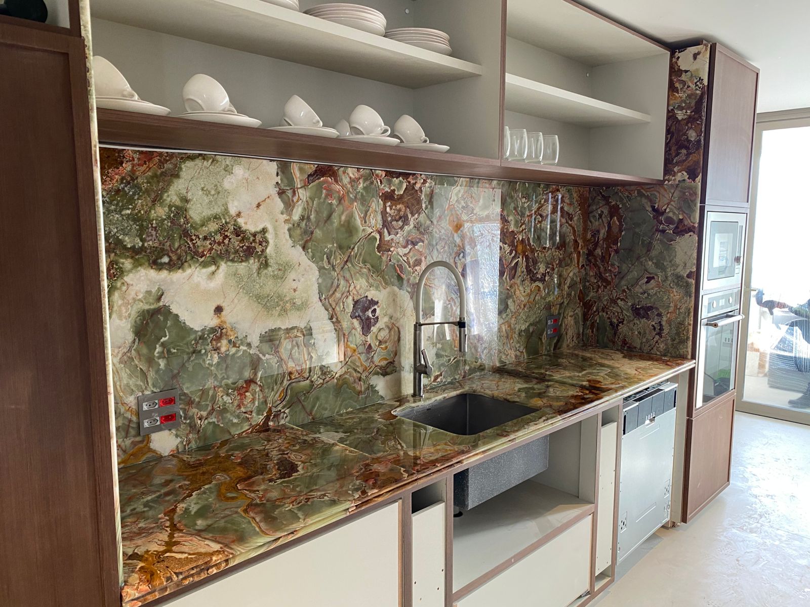 Painel de parede em ônix verde com veios casados integrado à bancada de cozinha